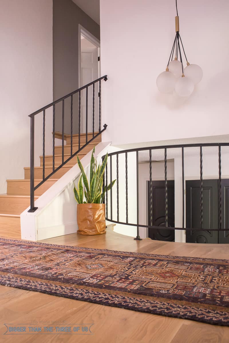 Vintage persian rug, leather DIY Planter, wood flooring and dark railing in this modern entryway 