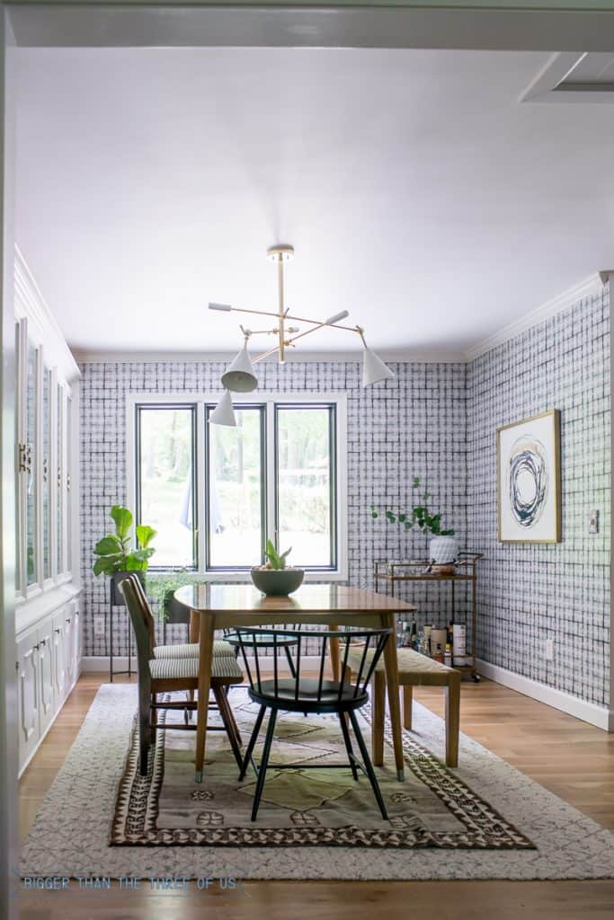 Layered rugs in dining room with mid-century accents, brass chandelier and wallpaper