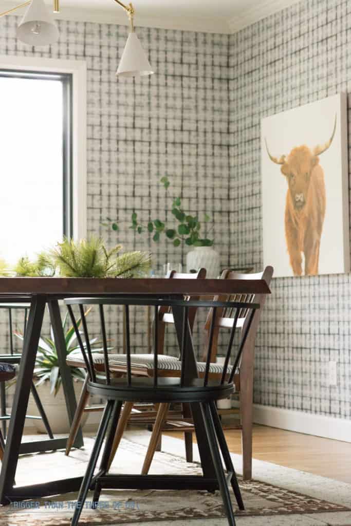 Wallpaper in dining room with midcentury furniture and a highland cow painting.