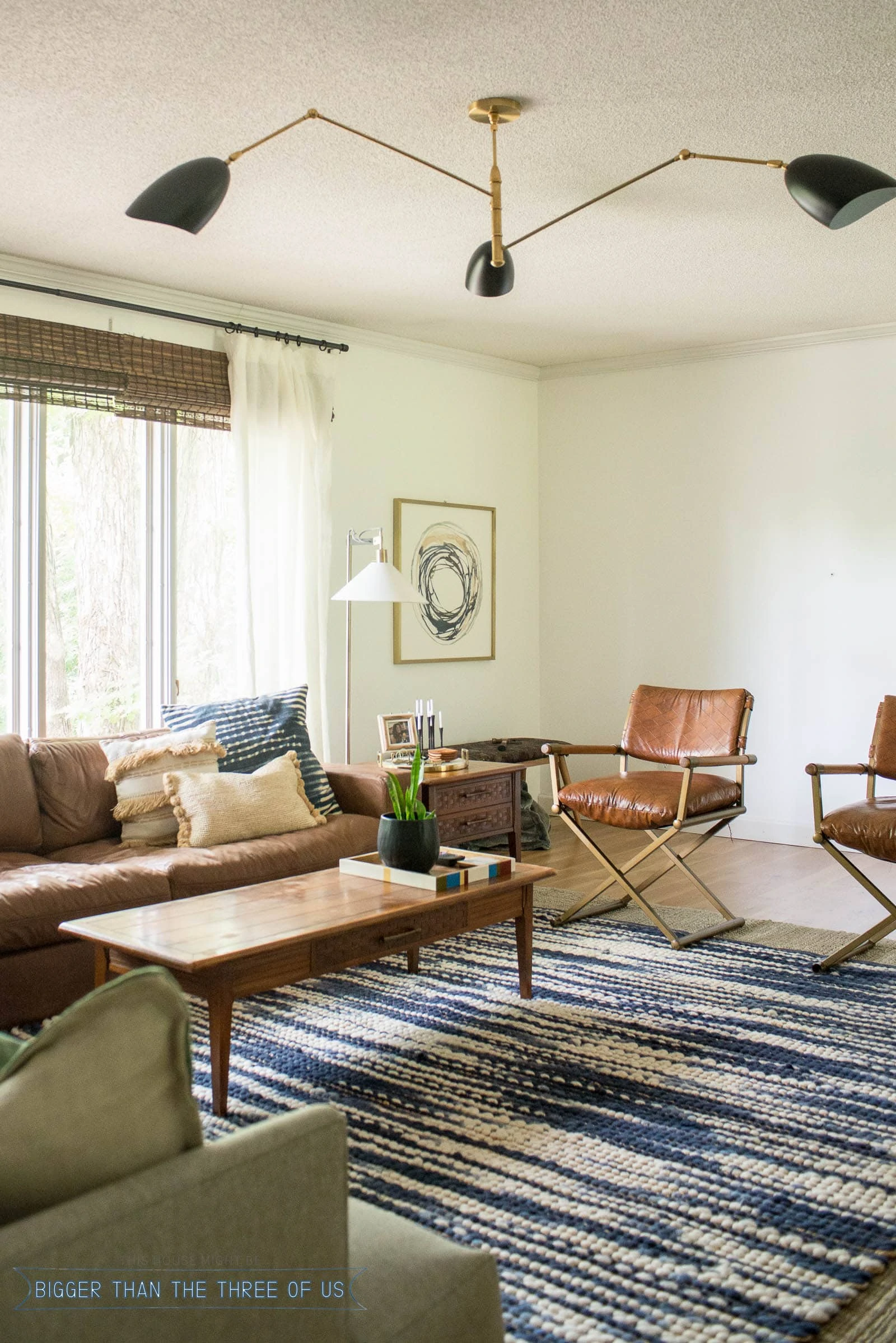 Couch in front of windows in living room. Brown leather couch with blue and white rug and mid-century furniture.