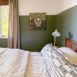 Cozy bedroom with green accent wall, lion artwork, and natural light from window. Perfect for relaxed, stylish stays.