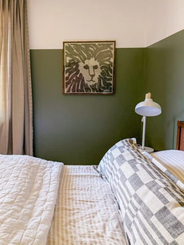 Cozy bedroom with green accent wall, lion artwork, and natural light from window. Perfect for relaxed, stylish stays.