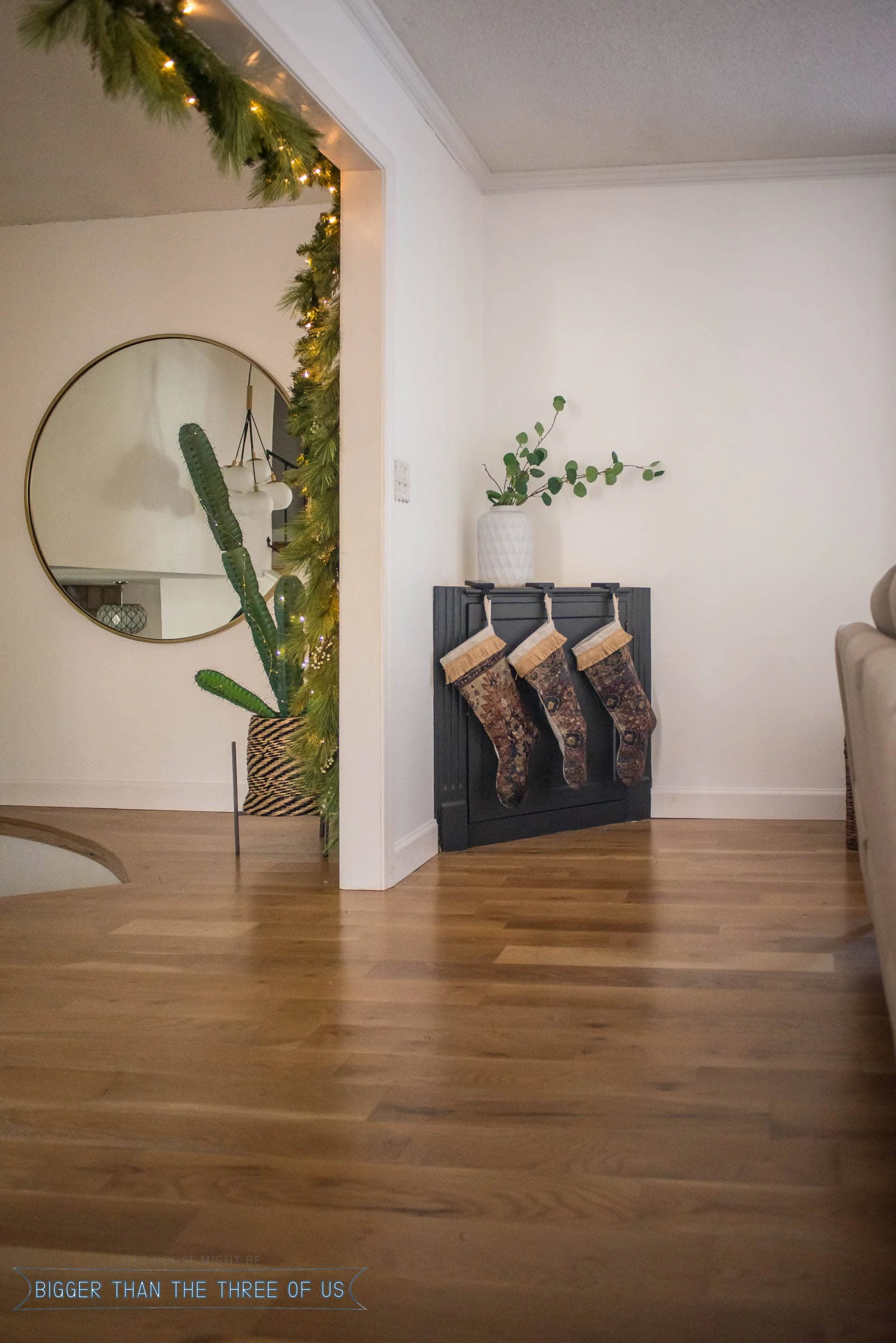 Stockings hung on corner cabinet and lights strung on cactus in living room.