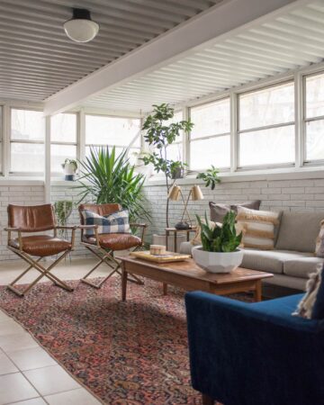 White painted brick sunroom with tile floor and an eclectic boho seating area with campaign leather chairs.