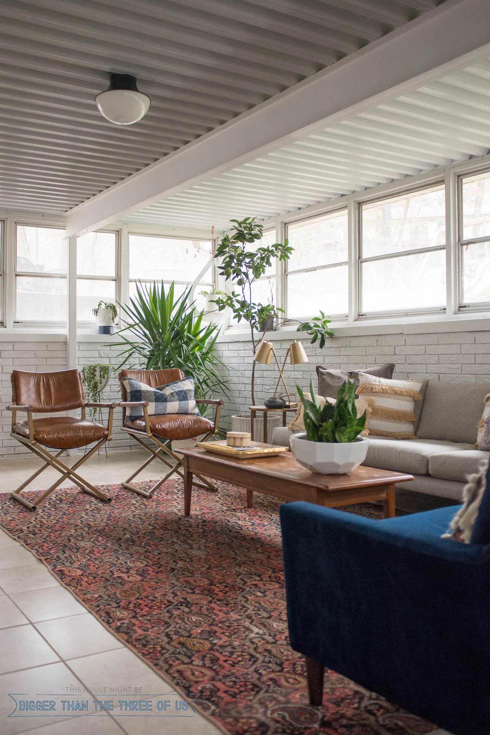 White painted brick sunroom with tile floor and an eclectic boho seating area with campaign leather chairs.