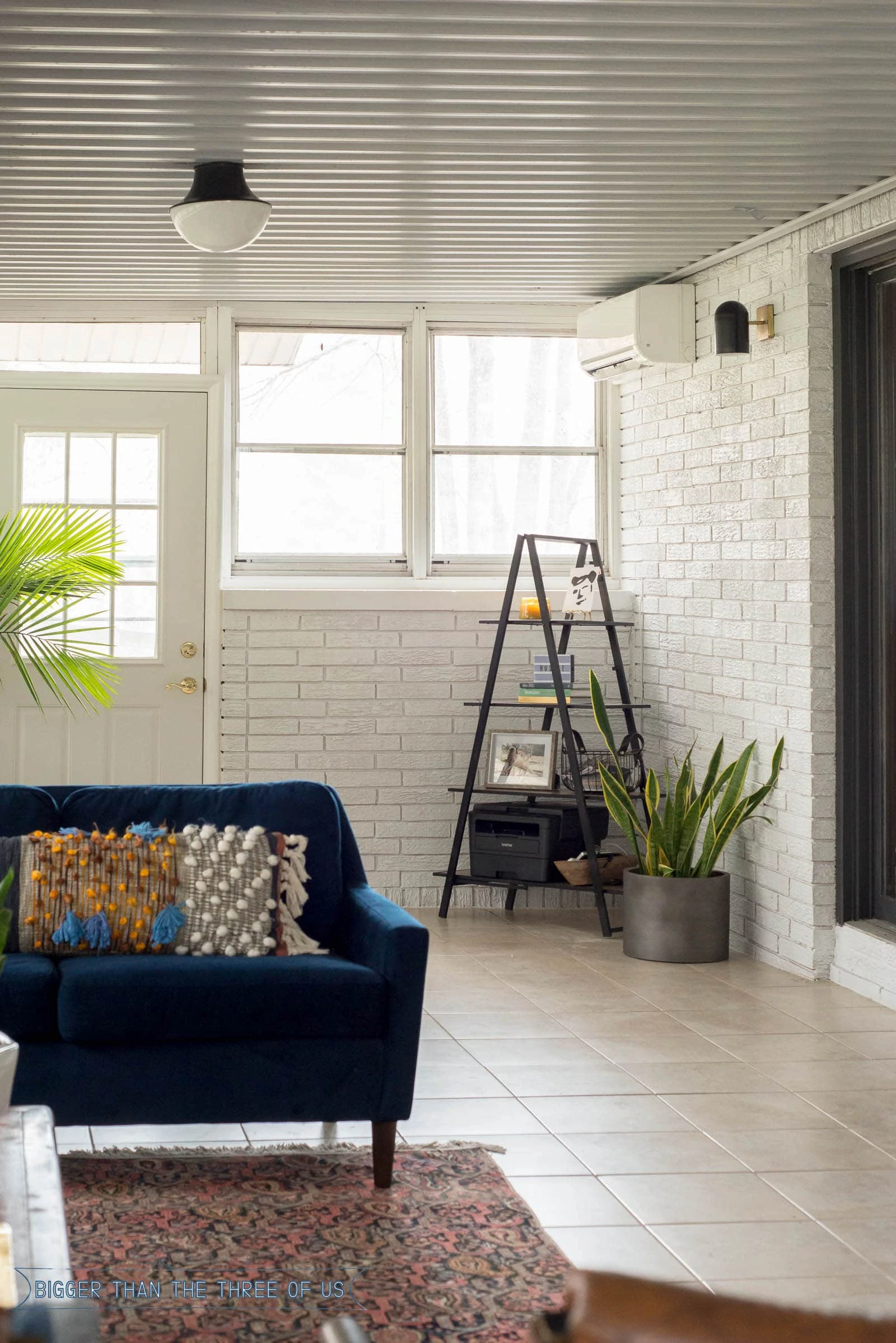 A frame shelf in the corner of a white painted sunroom with plants around it.