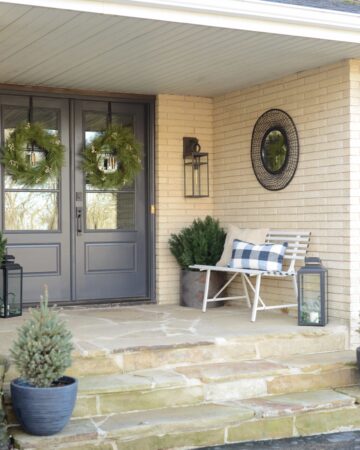 Double front doors on the front porch with white bench styled for winter.