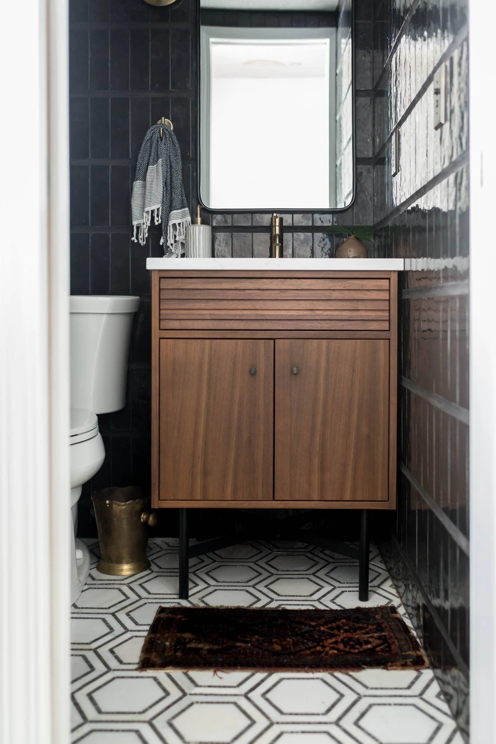 Black bathroom with black tile walls, walnut vanity and marble flooring plus powder room dimensions in this before/after