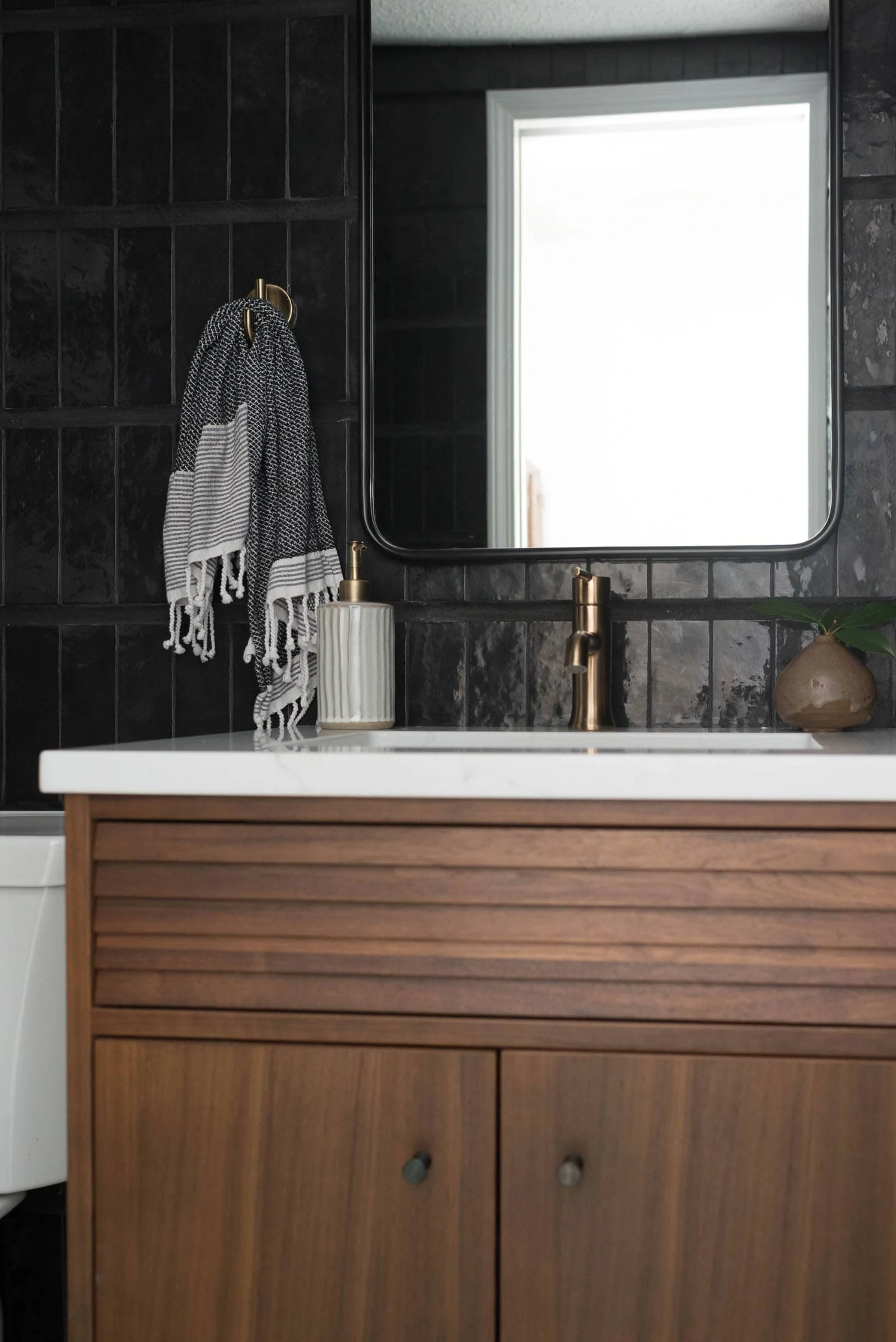 Walnut vanity in the powder bathroom with white quartz countertop and black wall tile