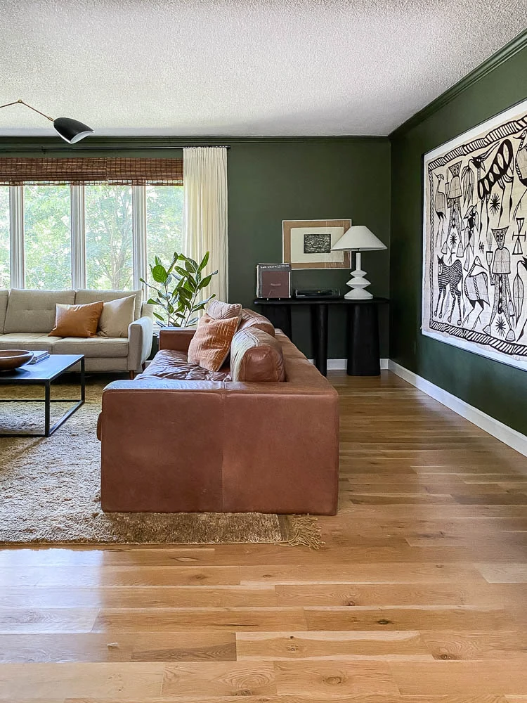 Forest Green living room with leather couch, mid-century accents and Korhogo art. 