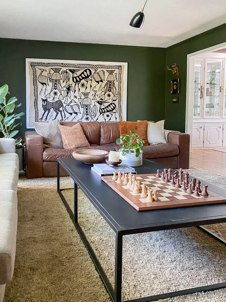 vintage African textile mounted on a canvas in a living room with green walls, leather couch and a shag rug. 