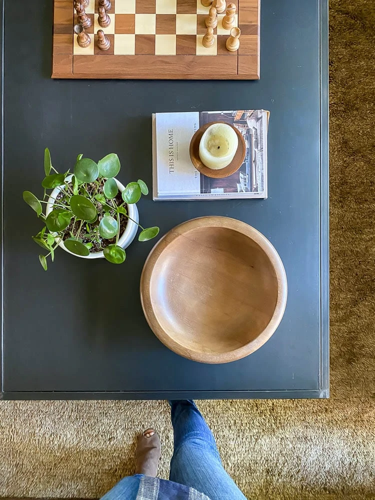 Coffee table decor ideas with a plant, wooden bowl, books, candle and chess board on coffee table