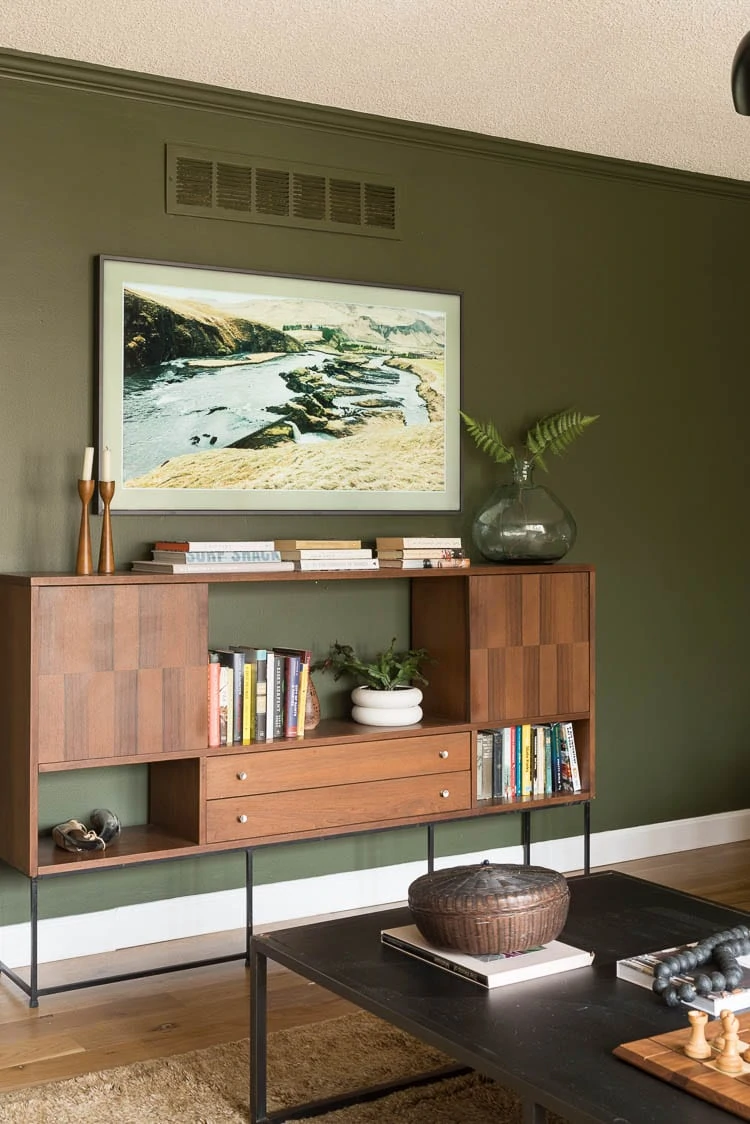 Green living room wall paint with mid century console filled with books