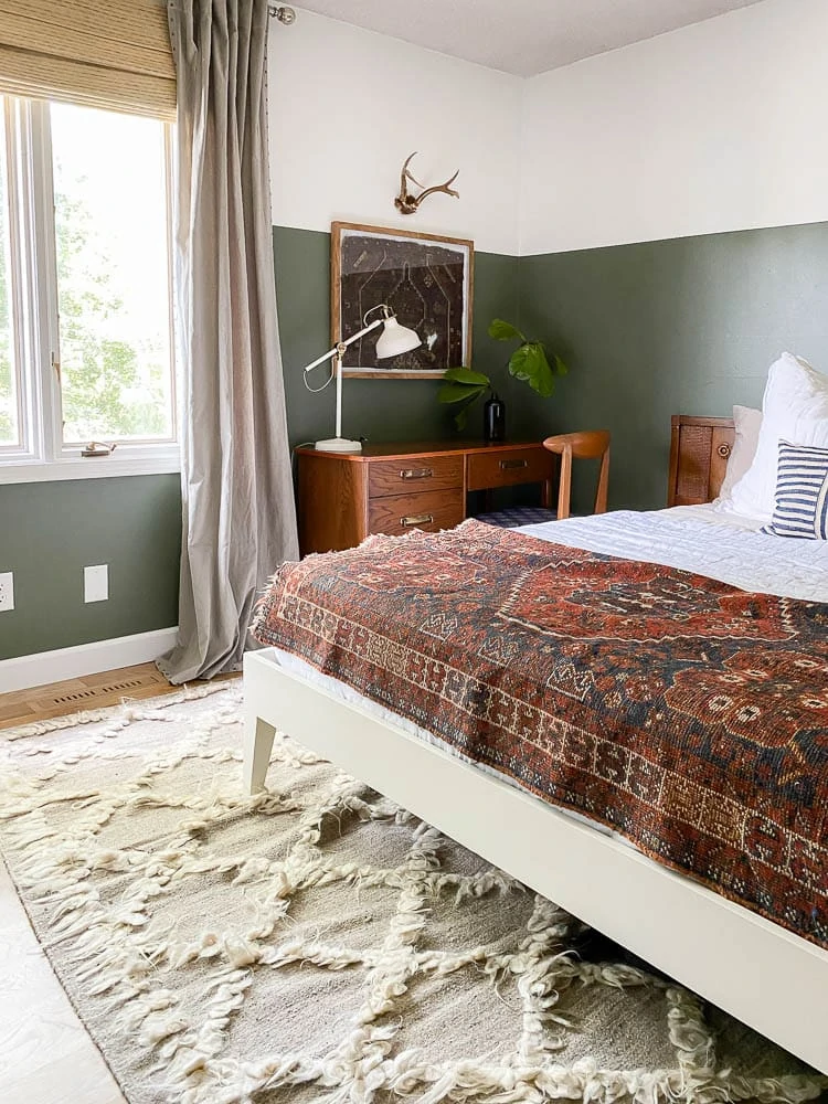 framed rug in bedroom with half green walls and bed