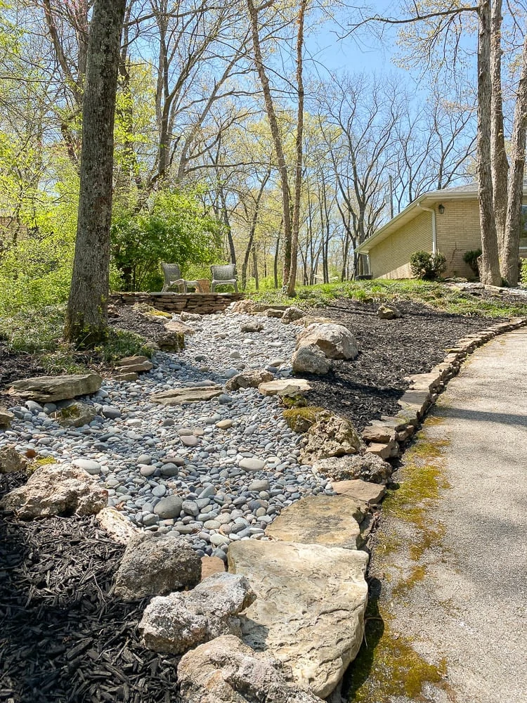 Rock landscaping showing a dry creek and how it ends at the driveway with a flagstone patio on top of the rock creek. 