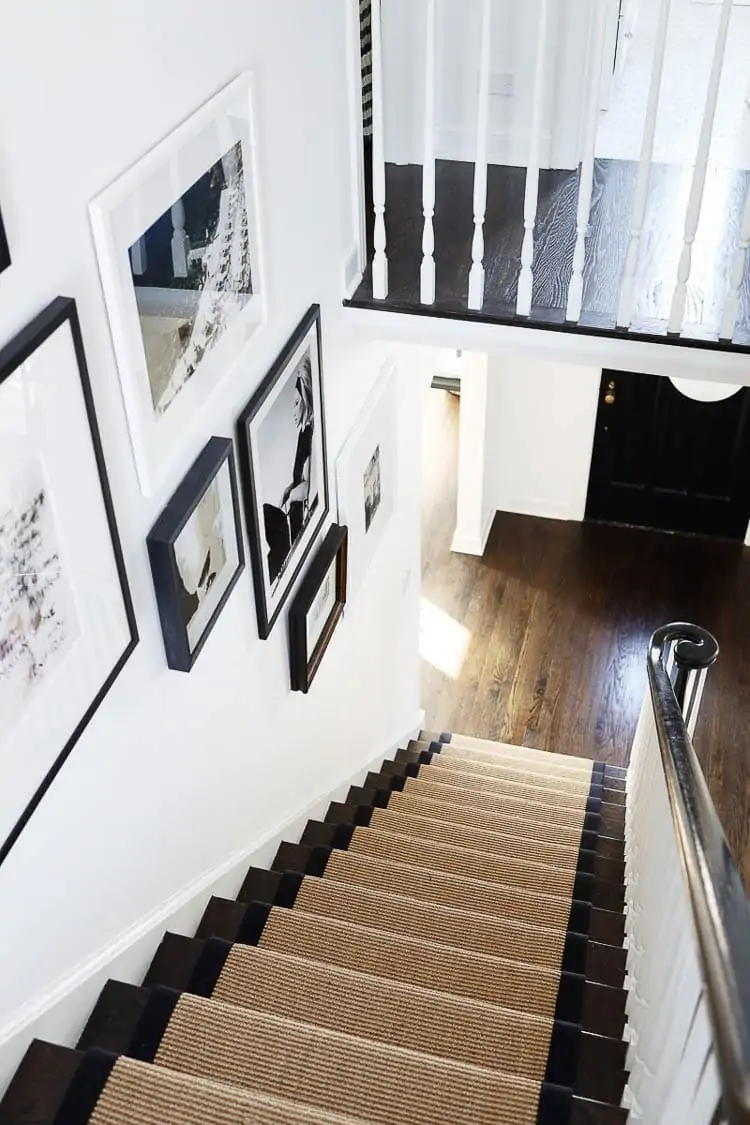 sisal carpet runner going down dark wood stairs with a black and white gallery wall on staircase wall 